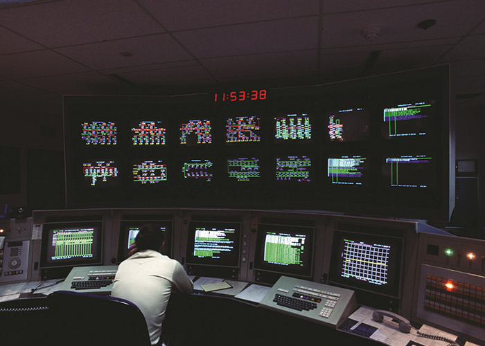 A man looking at computer screens in a dark control center.