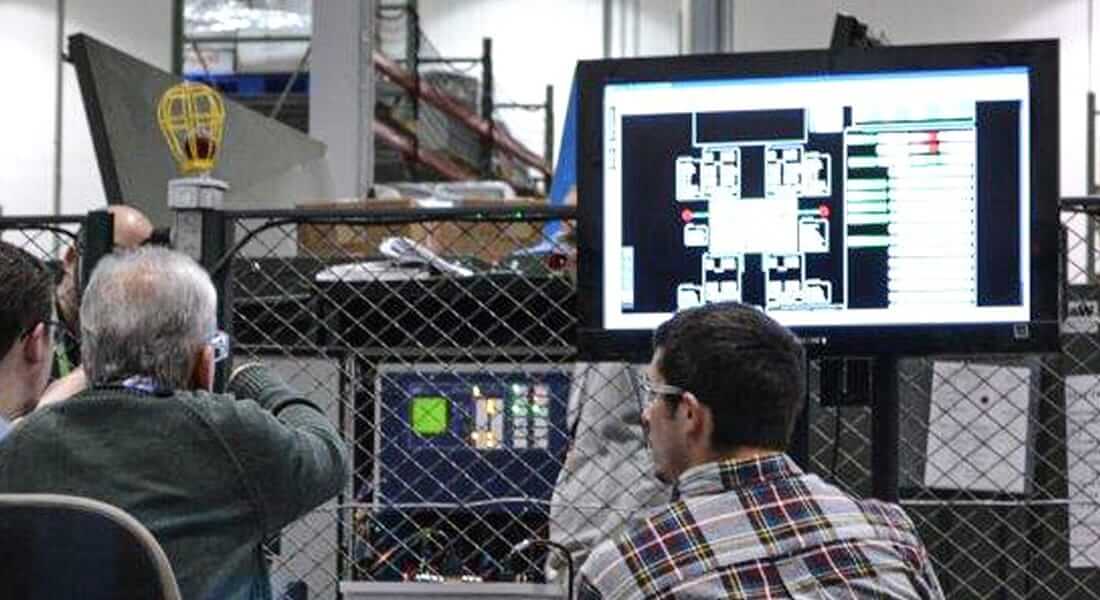 Two men sitting in a factory looking at a TV screen